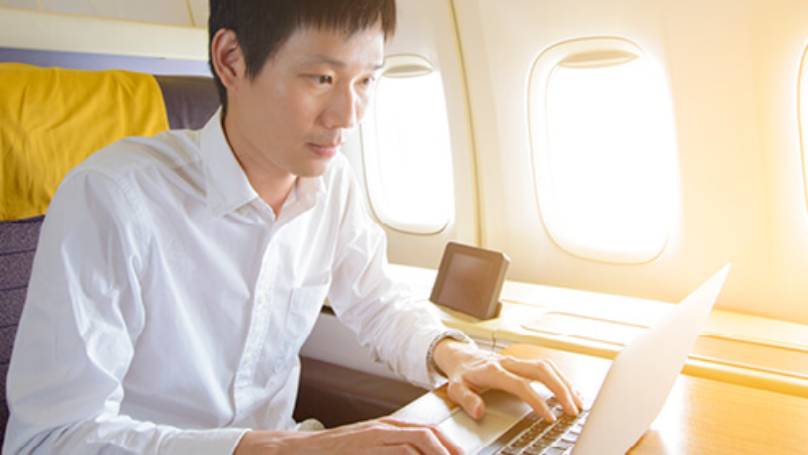 Man on plane in upgraded seating working on his laptop