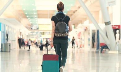 Woman wearing backpack walking at the airport pulling wheeled luggage behind her