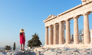 Woman in red dress and hat looking up at Greek ruins